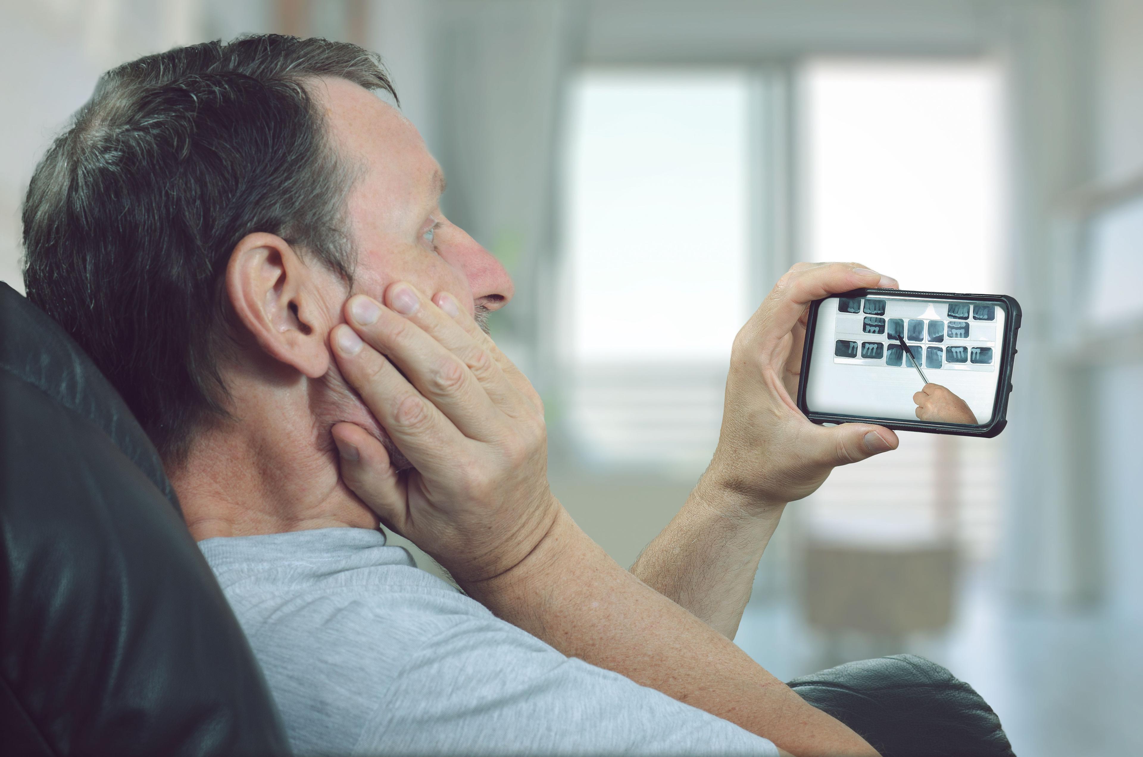 Man in pain viewing x-rays on a smartphone during teledentistry appointment